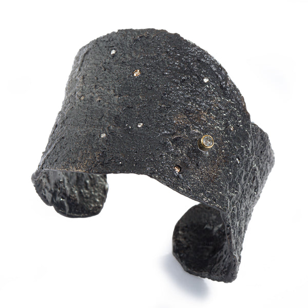 The Spark & Soul cuff in blackened sterling silver, adorned with small diamonds scattered across the surface and featuring an off-center, larger rose-cut diamond in an 18k yellow gold bezel, is a stunning statement piece reminiscent of a dark sky filled with stars. • Blackened sterling silver, diamonds 0.24 cts