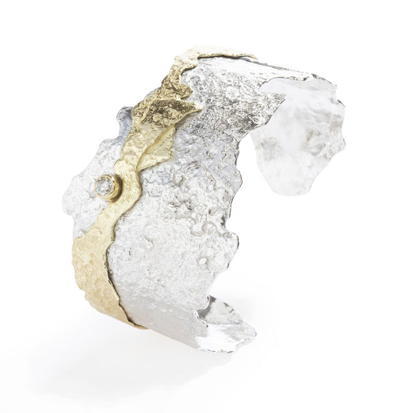 Good Vibes Textured Gold & Silver Cuff by Emanuela Duca - A cuff bracelet featuring a textured sterling silver wide band overlaid with a smaller layer of textured 18K yellow gold. Adorned with a stunning 4mm white/cognac diamond, this piece exudes sophistication and uniqueness. It's a statement accessory that adds a touch of elegance to any ensemble. One of a kind. Height: 1.60 inches.