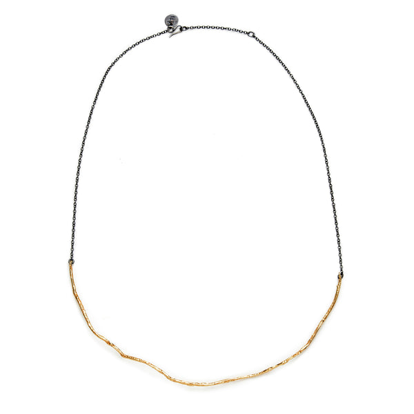 The Under a Tree necklace is a beautiful and refined piece that perfectly blends simplicity with character. This thin necklace features a solid, textured 18k yellow gold pendant, artfully suspended from a blackened sterling silver chain. The combination of rich, warm gold with the edgy, darkened silver creates a striking contrast that is both clean and elegant.