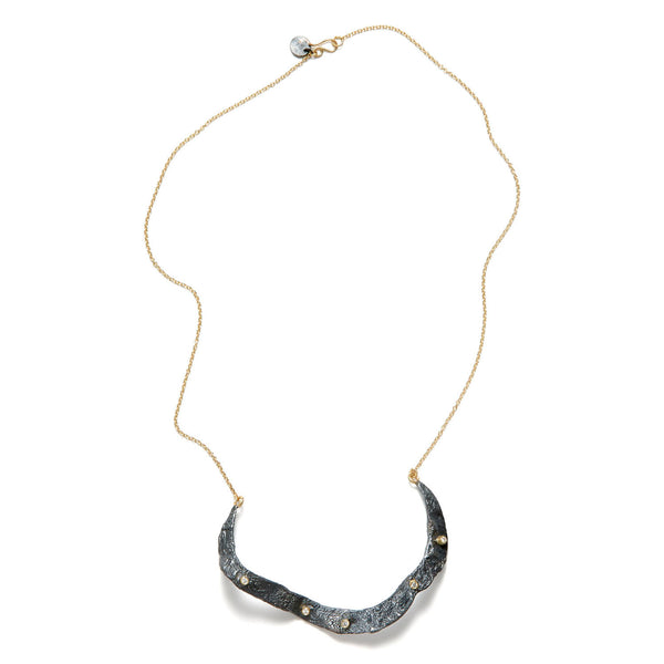 The Floating in the Dark necklace is a unique piece that exudes originality. It features a free-form, textured wavy element in blackened sterling silver, accented with diamonds set in 18k yellow gold bezels. These elements are beautifully complemented by an 18k yellow gold chain, making this necklace a striking blend of artistic design and luxurious materials. • Blackened sterling silver  • 18k yellow gold chain,&nbsp; diamonds ct: 0.15  • Length: 18 inches