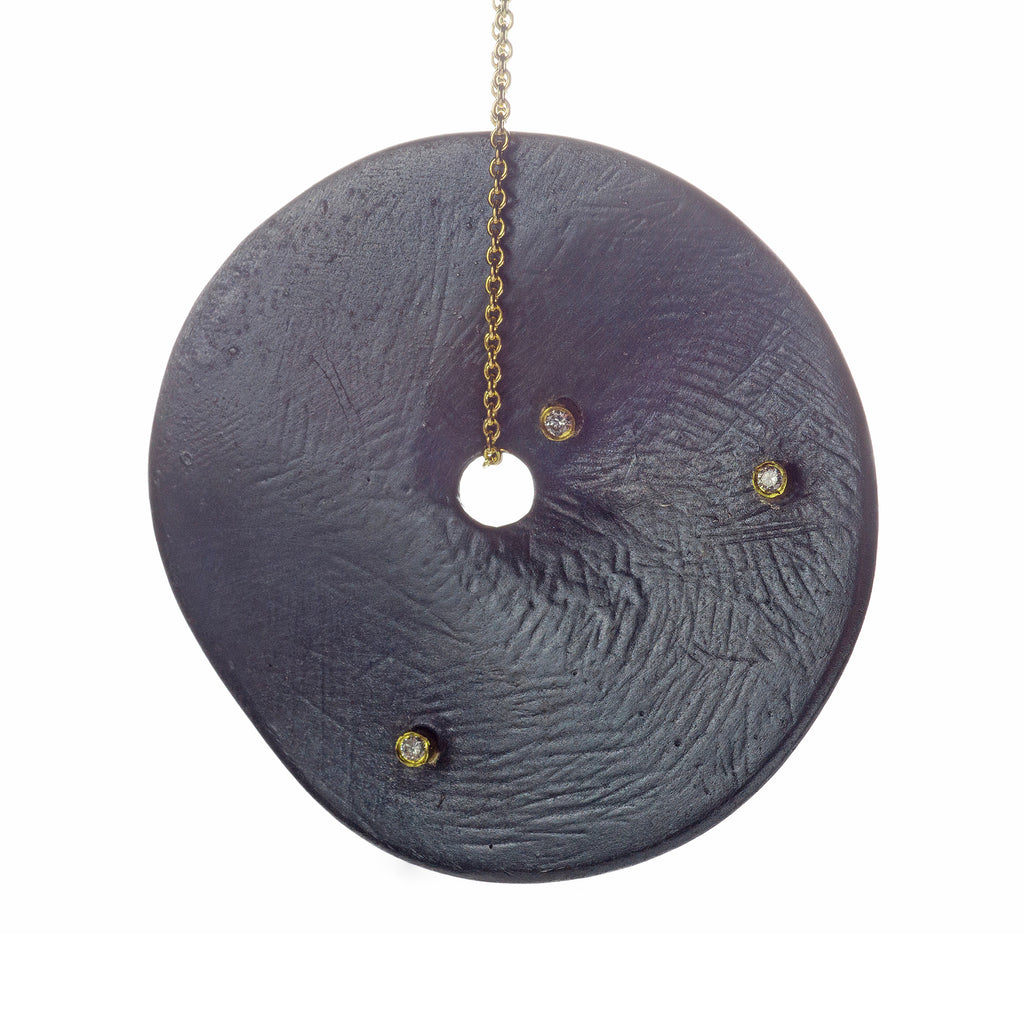 The Floating in the Dark large disc necklace is a striking statement piece that showcases bold personality. Accented by diamonds set in 18k yellow gold, this necklace combines the dramatic allure of large discs with the luxurious sparkle of diamonds and the warmth of gold, making it a standout accessory.  • Blackened sterling silver, 18k yellow gold chain, diamonds ct: 0.12