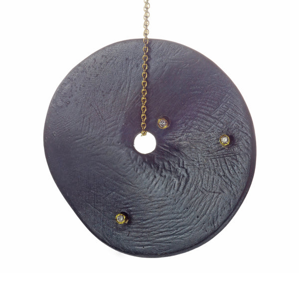 The Floating in the Dark large disc necklace is a striking statement piece that showcases bold personality. Accented by diamonds set in 18k yellow gold, this necklace combines the dramatic allure of large discs with the luxurious sparkle of diamonds and the warmth of gold, making it a standout accessory.  • Blackened sterling silver, 18k yellow gold chain, diamonds ct: 0.12